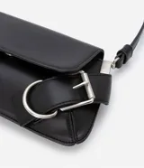 Cartera tipo baguette de tamaño pequeño, confeccionada en poliuretano color negro. Presenta una solapa frontal con detalles de hebillas metálicas decorativas en los laterales y un asa de hombro ajustable.