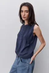 Blusa sin mangas color negro, de silueta fluida, con cuello redondo, detalle de alforzas en el frente y abotonadura parcial con botones visibles.