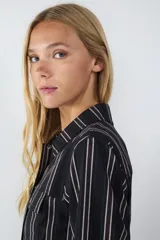 Camisa de manga larga confeccionada en popelina de algodón, con diseño de rayas verticales en tonos oscuros. Presenta cuello clásico, cierre frontal con botones metálicos y dos bolsillos frontales con solapa.