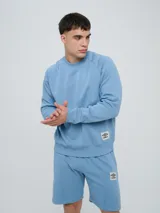 Buzo de felpa bordó, estilo relaxed, con cuello redondo y mangas raglán. Presenta puños y dobladillo acanalados, y una pequeña etiqueta con el logo de Umbro en el lateral inferior.