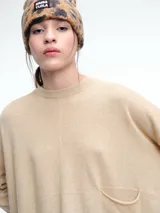 Sweater de tejido de punto color beige, con cuello redondo, hombros caídos y costura central vertical en el frente. Presenta un diseño de corte relajado, con largo asimétrico y aberturas laterales en el ruedo.