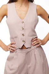 Chaleco color rosa pálido con escote en V y cierre frontal con cuatro botones marrones.