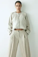 Pantalón tobillero de tiro alto en tejido arrugado color beige, con cierre de botón, bolsillos laterales y bajo ajustable con cordón.
