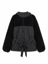 Campera negra con diseño combinado de tela técnica y textura de corderito en mangas y canesú superior. Cuenta con cierre frontal, capucha y lazo ajustable en la cintura.