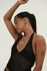 Top halter negro, ajustado al cuerpo, confeccionado en tejido de malla transparente con detalles brillantes o plateados en forma de líneas verticales. Presenta un escote pronunciado en V.