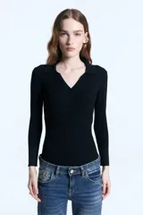 Chomba de punto acanalado color negro, con cuello polo, escote en V con botones y mangas 3/4 con puños de lurex. Presenta un diseño ajustado al cuerpo y un detalle metálico en la espalda.