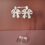 Par de aros colgantes con forma de moño color blanco nacarado y detalle de perla colgante.