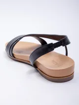 Sandalia baja de símil cuero color marrón, con doble cinta ancha cruzada sobre el empeine y tira elástica para ajuste en el tobillo.