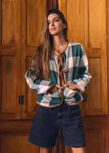 Saco a cuadros verde, blanco y negro con ribetes marrones, escote en V con lazos y mangas largas.