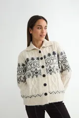 Saco de punto con cuello camisero, cierre frontal de botones oscuros y diseño de estampado nórdico en tonos gris y crema. Presenta textura de trenzas y terminaciones en tejido acanalado.