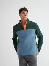 Buzo de polar verde y celeste con detalles en naranja, cuello alto con botones a presión y bolsillos laterales.