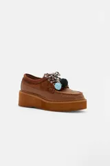 Zapato tipo mocasín de plataforma color bordó, confeccionado en una combinación de cuero liso y gamuza. Presenta cordones bicolores con detalle de borlas decorativas en el empeine.