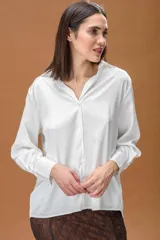 Camisa blanca de corte clásico y diseño holgado, con cuello camisero, cierre frontal de botones y mangas largas con puños anchos.