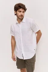 Camisa de manga corta en color blanco, con cuello clásico y cierre frontal de botones al tono. Presenta un diseño versátil de corte regular y textura liviana, ideal para looks frescos.