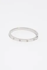 Pulsera rígida plateada con cierre de bisagra, decorada con incrustaciones en forma de corazón con pequeños cristales.