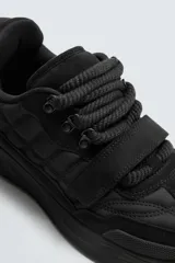 Zapatilla estilo skate de diseño robusto, confeccionada en una combinación de piezas de gamuza y material textil acolchado. Presenta un sistema de cierre con cordones gruesos y una tira de velcro en el empeine, junto con una suela de plataforma con relieve irregular.