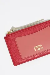 Billetera de cuero vacuno en color negro con bolsillo exterior en color naranja y tirador de cierre en color turquesa. Cuenta con logo de la marca estampado en dorado.