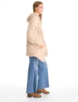 Cardigan de textura tipo sherpa o corderito, color beige, con diseño abierto sin botones, mangas largas con puños elásticos y capucha integrada. Presenta bolsillos laterales diagonales y un corte holgado.