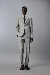 Blazer slim fit de color gris, con cuello de solapas de muesca, cierre frontal de dos botones, bolsillos laterales con solapa y bolsillo de vivo en el pecho. Presenta mangas largas con botones en los puños y aberturas en la espalda.