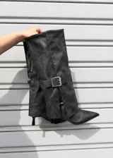 Botas de caña alta color gris, con diseño de solapa plegada y hebilla metálica plateada en el lateral. Presentan punta fina y taco kitten bajo.
