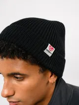Gorro tipo beanie de punto acanalado en color negro, con vuelta y etiqueta de la marca Umbro cosida en el lateral.