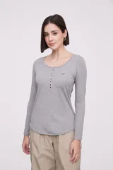 Remera blanca de manga larga, entallada, con cuello redondo y una hilera de botones en el frente. Incluye un pequeño bolsillo decorativo en el pecho.