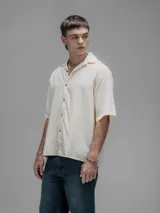 Camisa de manga corta color blanco roto, con cuello clásico y cierre frontal de botones.