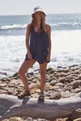 Vestido corto de algodón con pantalones cortos incorporados, color azul. Presenta un diseño liviano con escote redondo, tirantes finos y espalda cruzada. Incluye bolsillos de parche de gran tamaño en la parte delantera y un bolsillo con cierre en la espalda.