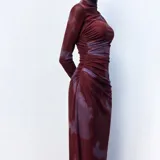 Vestido midi de microtul con diseño drapeado lateral, cuello alto y mangas largas. Presenta un estampado tipo tie-dye en tonos bordó y violeta.