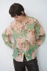 Camisa de manga larga con fondo verde y estampado floral en tonos rosados y beige, cuello redondo con pequeña abertura en V y cierre frontal con botones.