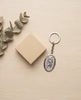 Llavero de acero con dije ovalado que presenta un relieve de San Cristóbal, santo patrono de los viajeros, con argolla circular de doble vuelta.