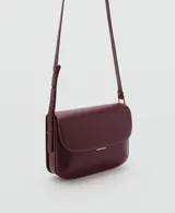 Bolso tipo bandolera de tamaño pequeño con acabado efecto piel en color bordó. Presenta una solapa frontal con cierre metálico a presión, costuras visibles en contraste y una correa larga ajustable con herrajes dorados.