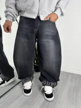 Pantalón de jean estilo baggy, color gris oscuro con efecto lavado, de corte holgado y diseño amplio. Presenta un detalle de bordado lineal en color blanco en el ruedo interno.