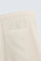 Bermuda de calce regular, color beige claro, confeccionada en tejido de mezcla de algodón con textura jacquard. Presenta cintura elástica ajustable con cordón, bolsillos frontales y un bolsillo trasero de vivo.