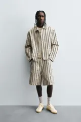 Cazadora de hombre de corte relajado, color beige claro con rayas verticales en azul oscuro con efecto desgastado o estampado. Presenta cuello solapa, manga larga, bolsillos de vivo en cadera y cierre frontal con botones a presión.