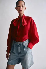 Camisa de ZARA Woman Collection confeccionada en hilatura con mezcla de lyocell, de color blanco marfil. Presenta cuello redondo, escote en V con lazadas en el mismo tejido, manga larga con puño y bajo recto.