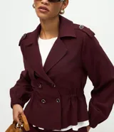 Campera de estilo trench corto en color bordó, con cuello solapa, cierre cruzado con botones, detalle de charreteras en los hombros, cintura elástica marcada y mangas largas con puños ajustados.