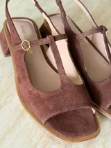 Sandalia de gamuza color marrón, con diseño tipo T-strap, taco cuadrado bajo y tira ajustable al talón con hebilla metálica dorada.