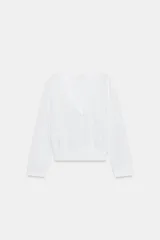Top de algodón blanco de manga larga, con escote en V y cierre frontal con botones. Presenta bajo y puños en rib elástico.