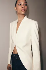 Blazer tipo frac de corte largo y diseño sin solapa. Presenta mangas largas con abertura, falsos bolsillos de vivo en el delantero y bajo asimétrico. Cuenta con cierre frontal mediante gancho metálico y forro interior a tono.