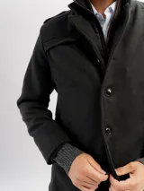 Tapado de paño negro con pechera de nylon desmontable, cierre frontal y puños tejidos acanalados.