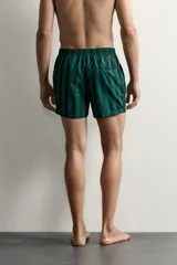 Short de baño confeccionado en tejido técnico, con diseño de rayas verticales en color verde y negro. Cuenta con cintura elástica ajustable con cordón, bolsillos laterales y bolsillo trasero con vivo, además de forro interior.