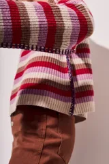 Sweater de lana con rayas horizontales en tonos rojo, rosa, beige y marrón. Presenta costuras decorativas en los laterales y puños en color violeta.