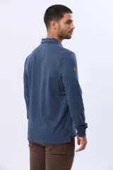 Remera polo de manga larga confeccionada en tejido jersey, con cuello clásico y cierre frontal de tres botones. Presenta un diseño liso con un pequeño logo bordado en el pecho y una etiqueta decorativa en el ruedo.