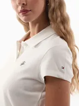 Chomba blanca de piqué de algodón regenerativo con corte slim, cuello tipo polo, cartera de dos botones, logo Tommy Hilfiger Script bordado en el pecho y bandera de Tommy Hilfiger bordada en la manga.