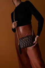 Bandolera negra de cuero sintético con diseño matelassé, cierre superior con cremallera dorada, correa de cadena dorada y borla decorativa.