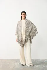 Poncho triangular tejido con diseño de rayas verticales en tonos crudo, marrón y negro, con detalle de hilo de lurex brillante y terminación de flecos largos en todo el borde.