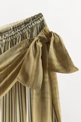 Pantalón de tiro medio con estampado de rayas verticales, cintura elástica y bajo abullonado con elástico. Presenta una superposición de tejido tipo pareo con lazada lateral ajustable en contraste.