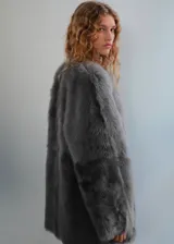Campera de piel sintética con pelo largo color gris, diseño recto, cuello redondo y manga larga.