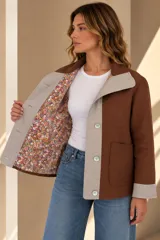 Campera marrón de lino con diseño bicolor, con una franja central gris claro que incluye botones de nácar. Cuenta con cuello alto, mangas largas con puños grises, bolsillos frontales aplicados y silueta amplia.